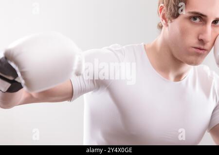 Con una camicia bianca, un giovane con guanti da boxe è pronto a dare un pugno, la sua espressione è seria e si è concentrato sulla sfida Foto Stock