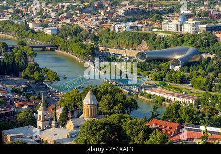 Vista di Tbilisi, dalla fortezza di Narikala. Fiume Mtkvari, antica chiesa ortodossa Sioni, Ponte della Pace e Parco Rhike, Teatro musicale e sala esposizioni Foto Stock