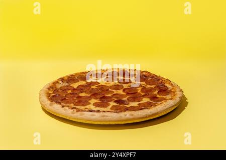 Pizza al peperoni incentrata su sfondo giallo in studio con spazio per copie Foto Stock