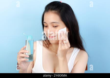 Giovane donna asiatica che si tocca la faccia con un tampone usando acqua micellare e per la rimozione del trucco, routine quotidiana per la cura della pelle Foto Stock
