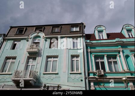 Elegante architettura dell'inizio del XX secolo in colori pastello situata in una vivace area urbana sotto un cielo nuvoloso Foto Stock