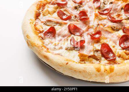 Primo piano di una pizza appena sfornata con peperoni, prosciutto e funghi su sfondo bianco. Foto Stock