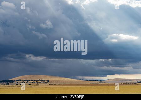 Vista lontana dei raggi del sole che si infrangono attraverso nuvole scure su una collina arida e arida a Campbelltown nel Victoria centrale, Australia Foto Stock