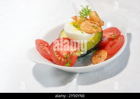 Mezza avocado farcita con uova sode e gamberetti, servito con pomodoro e guarnigione di prezzemolo su un piatto bianco, snack a basso contenuto di carboidrati come colazione o antipasto, Foto Stock