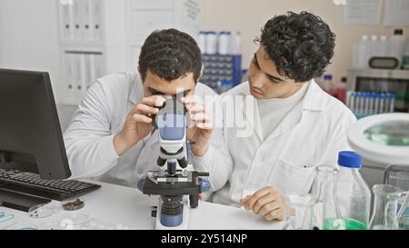 Due uomini in camice bianco collaborano utilizzando un microscopio in un moderno ambiente di laboratorio. Foto Stock