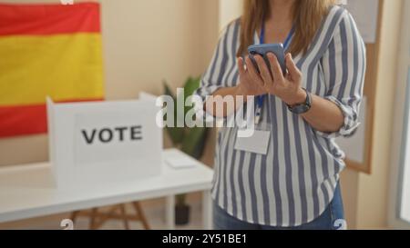 Donna che usa il telefono in una sala del college elettorale con bandiera spagnola e cabina elettorale Foto Stock