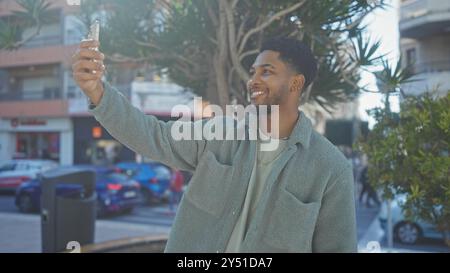 Un uomo nero sorridente si fa un selfie in una strada soleggiata. Foto Stock