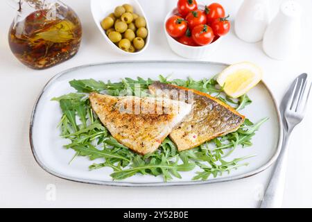 Filetto di dorado fritto con pelle croccante. Rucola, pomodori ciliegini, olive, limone e olio d'oliva. Piatto tradizionale mediterraneo. Sfondo bianco. Selez Foto Stock