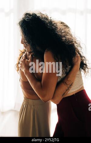 Due donne condividono un abbraccio intimo, illuminato da una luce naturale soffusa Foto Stock