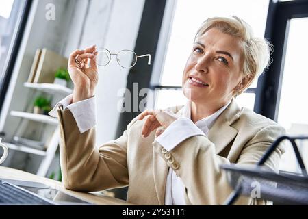 Una donna elegante esprime fiducia mentre tiene gli occhiali in un ambiente moderno. Foto Stock