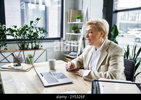 Una donna adulta in abiti alla moda partecipa a una discussione virtuale presso una scrivania ben illuminata. Foto Stock