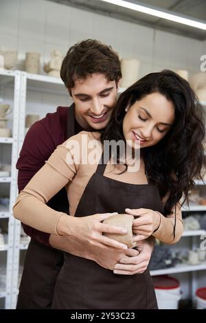 Un paio di persone modellano con gioia l'argilla mentre si abbracciano in un vivace studio di ceramica. Foto Stock