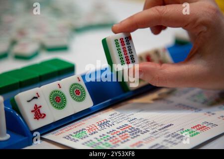 Una persona in mezzo all'azione che usa le mani per tenere la tessera mahjong nel popolare gioco Foto Stock