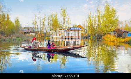 L'immagine mostra una scena sul lago dal, con una donna che canta su una barca che trasporta due bambini, circondata da case galleggianti e dai riflessi vibranti nell'acqua. Foto Stock