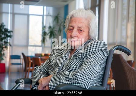 Ritratto di donna anziana seduto in una sedia a rotelle, guardando la telecamera. Foto Stock