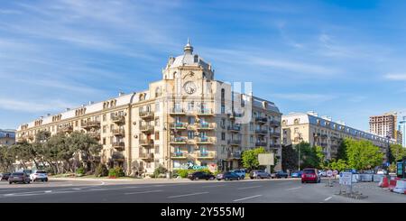 Baku, Azerbaigian - 10 maggio 2024: Al viale 8 novembre spicca uno splendido edificio storico con dettagli intricati. Le auto passano, mentre il verde dà vita al paesaggio urbano sotto il cielo azzurro Foto Stock