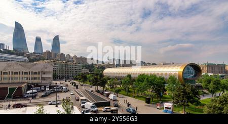 Baku, Azerbaigian - 4 maggio 2024: Il Museo nazionale dei tappeti dell'Azerbaigian presenta un'architettura unica, mentre le iconiche Torri delle fiamme si innalzano maestosamente sullo sfondo in un vivace paesaggio urbano Foto Stock