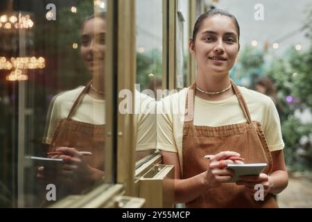 La giovane cameriera caucasica sorride leggermente e si appoggia alla porta dorata mentre posa per un ritratto Foto Stock