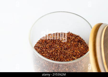 tè rooibos in un vaso di vetro aperto con tappo in legno isolato su sfondo bianco Foto Stock