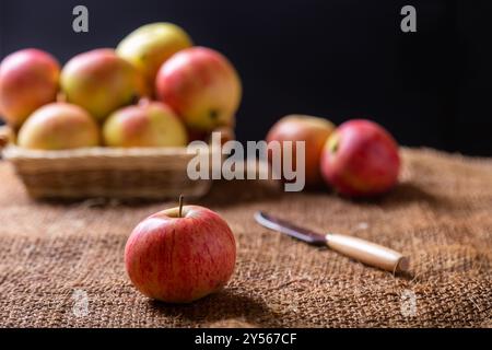 Mele mature sul burlap e in un cesto su fondo nero. Stile rustico, primo piano. Foto Stock