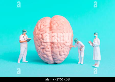 Tre figurine di chirurgo in miniatura che analizzano un modello cerebrale, raffigurano la ricerca medica e i concetti scientifici su un vivace sfondo blu. Foto Stock