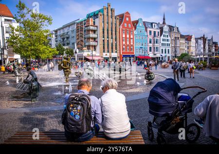 Rostock, Germania. 19 settembre 2024. I passanti siedono in Piazza dell'Università di fronte alla fontana della joie de vivre. University Square si trova sull'ex piazza del mercato della nuova città costruita nel 1252. L'edificio principale dell'università, fondata nel 1419, si trova qui. Crediti: Jens Büttner/dpa/Alamy Live News Foto Stock