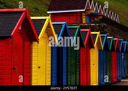 Immerse nella luce soffusa, le colorate capanne sulla spiaggia di Whitby creano una prospettiva sorprendente, la loro simmetria si distingue contro la spettacolare costa. Foto Stock