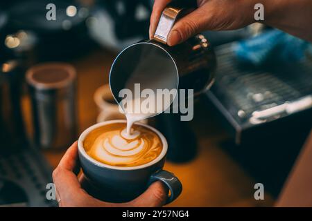 Un caffè che viene versato in una tazza blu in un caffè a Melbourne, Australia. Il barista sta sta preparando la latte art con il latte montato. Primo piano. Foto Stock