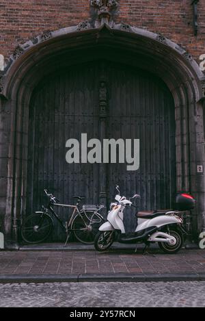 Uno scooter e una bicicletta davanti a una grande porta ad arco in legno a Bruges, Belgio. Foto Stock