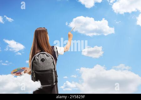 Foto retrovisiva di una studentessa che dipinge nuvole nel cielo con un pennello e una tavolozza Foto Stock