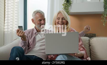 Felice anziano maturo coppia caucasica anziano maturo moglie anziano marito maschio in possesso di carta di credito pagamento remoto donna uomo famiglia parlare Foto Stock