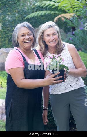 Sorridenti amiche di sesso femminile multirazziale con piante in vaso e giardinaggio all'aperto Foto Stock