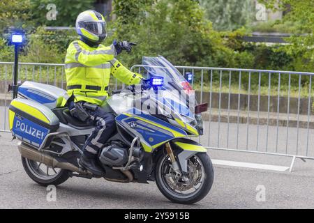 Un poliziotto in un gilet ad alta visibilità guida una moto della polizia con luci blu e mostra la strada su una strada a cordoncino, Stoccarda, Baden-Wuertt Foto Stock