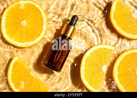 Flacone contagocce con siero o olio essenziale per illuminare il viso e fette di agrumi arancioni sullo sfondo dell'acqua, vista dall'alto. Idratante vit. Organica Foto Stock