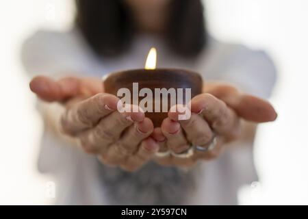 Primo piano di una candela splendidamente illuminata tenuta delicatamente nelle mani di una donna Foto Stock