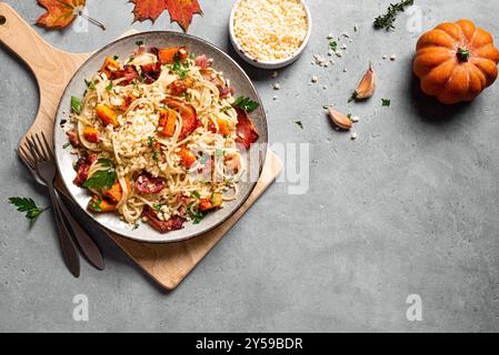 Pasta di zucca e pancetta con parmigiano grattugiato. Spaghetti fatti in casa, pasta di zucca su sfondo grigio in cemento, spazio copia. Cibo stagionale autunnale. P Foto Stock