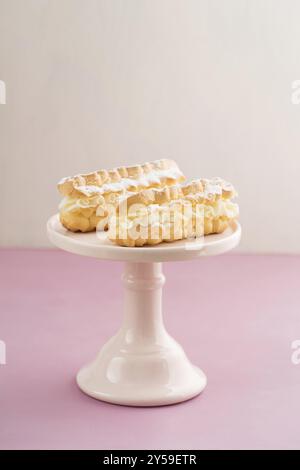 Eclairs con crema di burro ripieno su una torta rosa stand Foto Stock