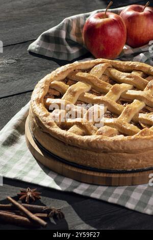 Tavolo da cucina con una torta di mele su un tagliere di legno e un asciugamano, frutta di mele e cannella, con luce naturale. Torta classica tradizionale Foto Stock