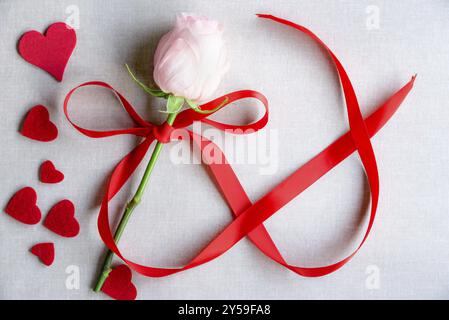 Idea di tessera da giorno per donne con una rosa legata con nastro a forma di numero 8, circondata da molti cuori rossi, su uno sfondo in tessuto vintage Foto Stock