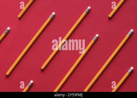 Concetto di formazione con un mucchio di matite di legno gialle disposte simmetricamente, come un motivo su un foglio di carta rosso Foto Stock