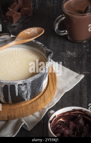 Ingredienti per il contesto della cioccolata calda, con latte in una pentola rustica, cioccolata, cacao e una tazza di cioccolata calda, su un tavolo nero Foto Stock