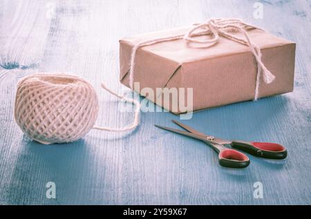 Confezione regalo fatti in casa, avvolto nel classico carta marrone, sfera di stringa e la forbice su un tavolo blu Foto Stock