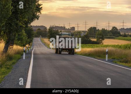 Immagine del giorno di raccolta con un camion carico di grani che percorre una lunga strada di campagna, al tramonto, vicino alla città di Schwabisch Hall, Germania, Europa Foto Stock