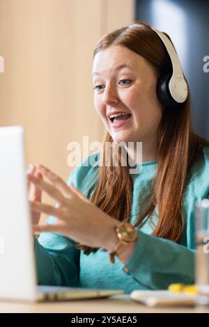In ufficio, indossando cuffie, videochiamate da donna su un laptop e lavorando in remoto Foto Stock