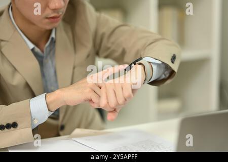 Primo piano, giovane uomo d'affari con abbigliamento formale che controlla il tempo su uno smartwatch. Concetto di gestione del tempo Foto Stock