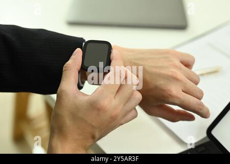 Primo piano, giovane uomo d'affari con abbigliamento formale che controlla il tempo su uno smartwatch. Concetto di gestione del tempo Foto Stock