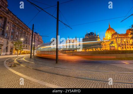 Budapest, Ungheria: 8 luglio 2024: Linea tram motion blur. Piazza Lajos al crepuscolo. Il Parlamento sullo sfondo. Scatto con esposizione lunga. Foto Stock