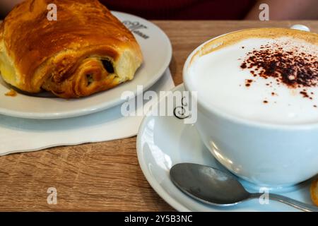 (Croissant al cioccolato (pain au chocolat) e cappuccino su un piatto in una panetteria - tradizionale colazione parigina a Parigi, Francia Foto Stock