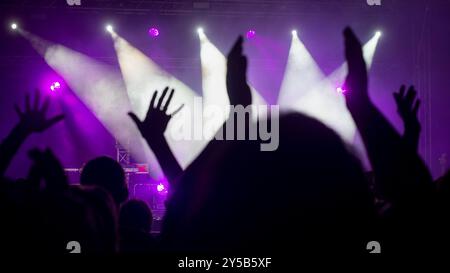 Le persone alzano le mani ascoltando musica dal vivo davanti alla scena del nightclub con illuminazione viola Foto Stock