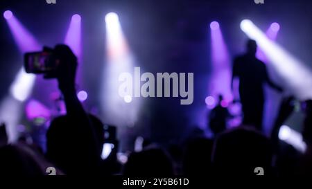 Persone affollate si sagomano scattando foto durante un concerto di musica dal vivo. Musicisti sfocati sul palco illuminato Foto Stock